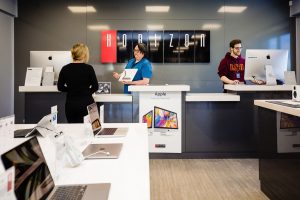 A wide shot of the Horizon Retail Store. The worker on the left shows products to a customer.